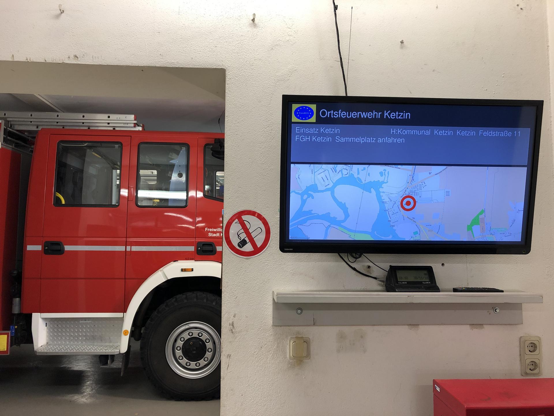 Alarmdisplay im Gerätehaus Ketzin neben einem Feuerwehrfahrzeug